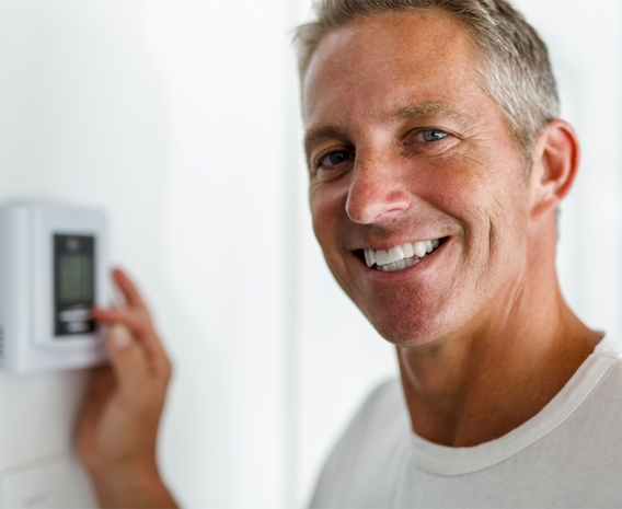 Smiling man in white t-shirt, standing in front of thermostat
