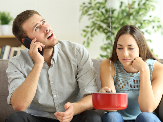 Man and woman sitting on couch with water leaking from ceiling into red pot